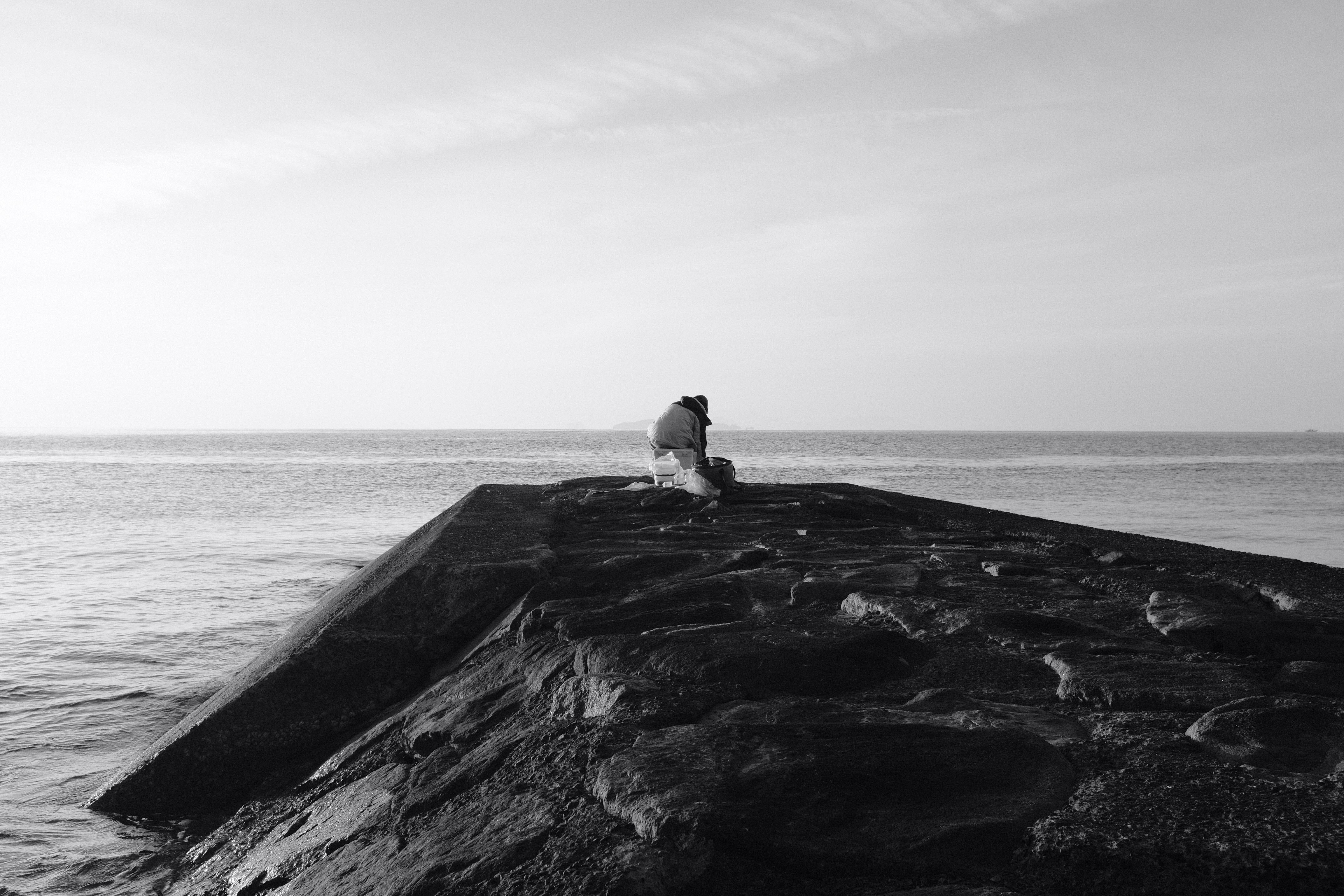 grayscale photo of couple standing on rock near sea